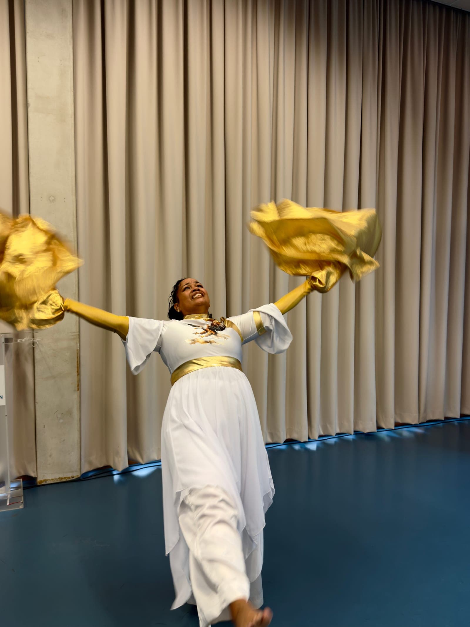 A dancer with arms spread wide, gold flags in both hands