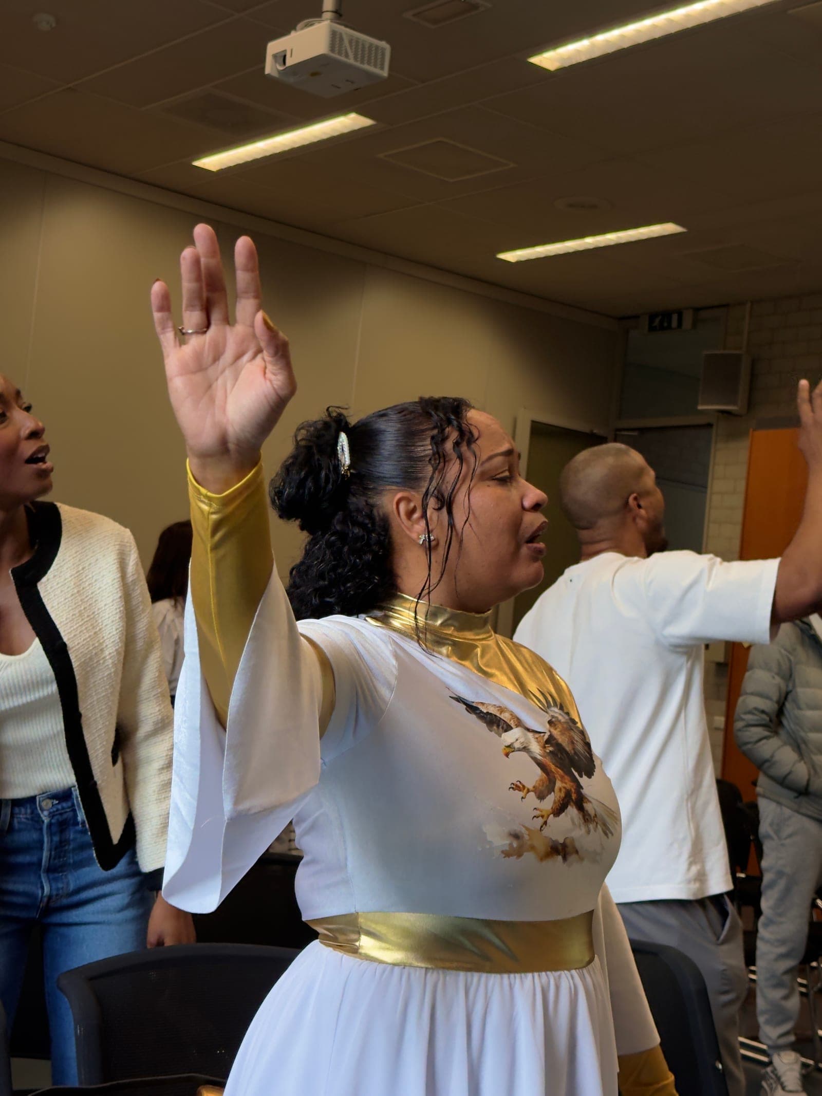 A worshipper in white and gold with her hand raised during praise